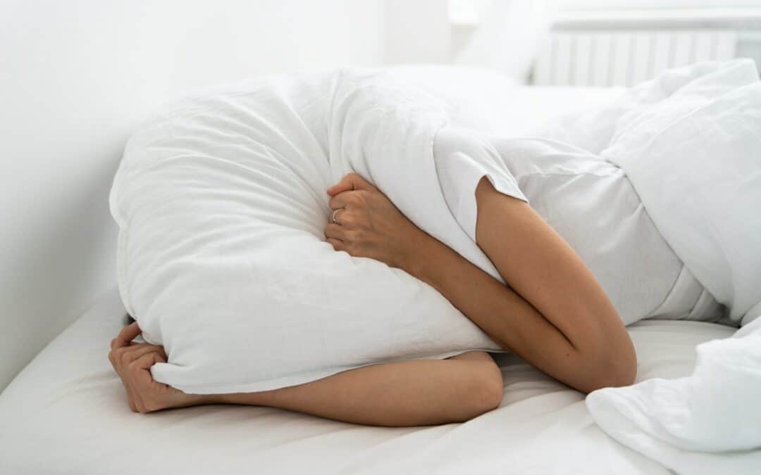 Depressed woman lying alone on bed covering head with pillow feeling mental health, loneliness