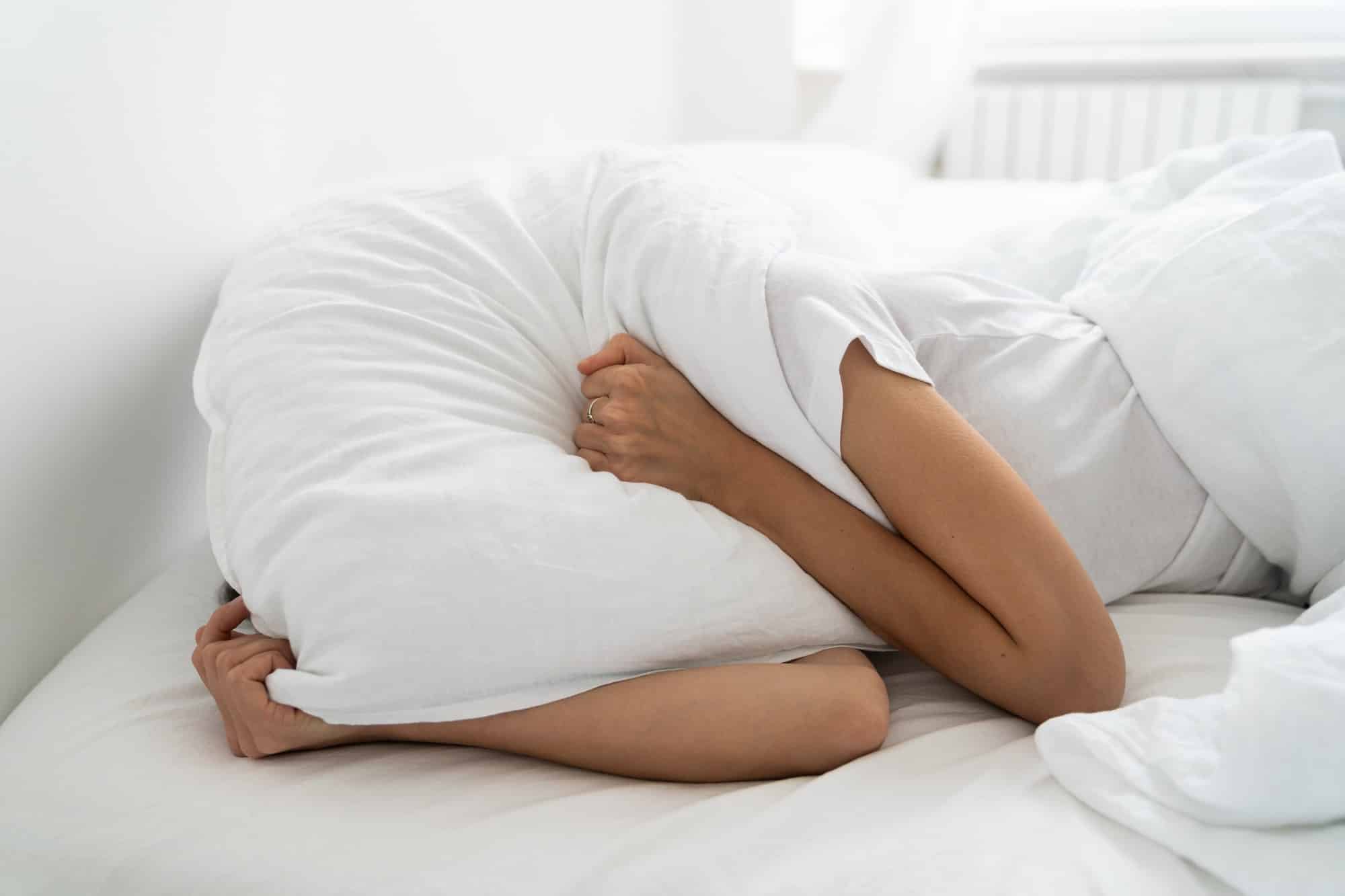 Depressed woman lying alone on bed covering head with pillow feeling mental health, loneliness